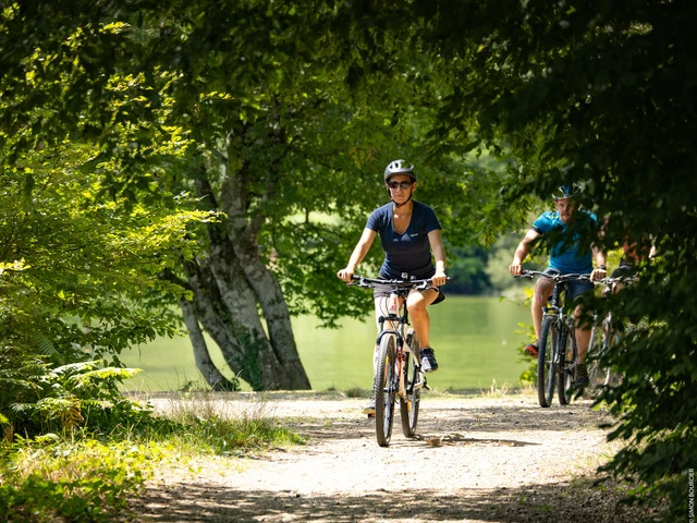 deux personnes faisant du vélo sur un sentier ombragé au bord du lac de Mervent