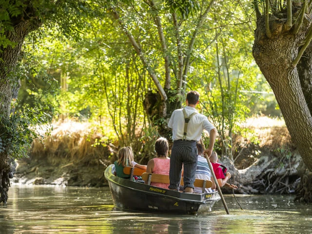 une barque maraichine transportant un batelier et 4 personnes sur un canal bordé d'arbres dans le marais poitevin